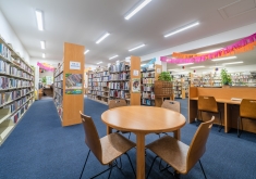 Photo of library, showing a round table with chairs, computer stations, and bookshelves